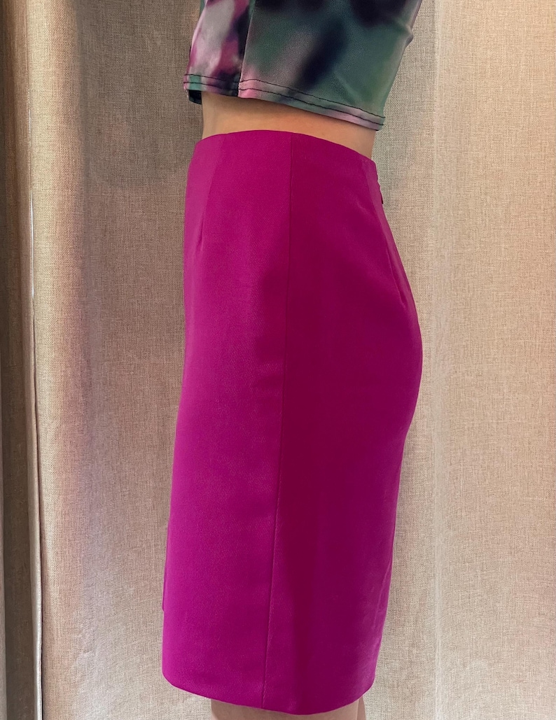 May include: A high-waisted, knee-length pencil skirt in a vibrant magenta pink color. The skirt features a smooth, solid fabric construction with a clean, straight silhouette and a subtle side seam detail, ending just above the knee.