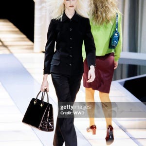 May include: A black button-down blazer with matching black trousers and a black structured handbag. The outfit is paired with black shoes and dark sunglasses worn on the head. A second outfit features a lime green jacket, a maroon skirt, and yellow tights.