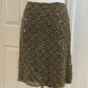 May include: A knee-length skirt featuring a black base with a repeating geometric pattern in yellow and dark red. The fabric is embellished with small, scattered silver sequins that catch the light, creating a subtle shimmer across the surface.