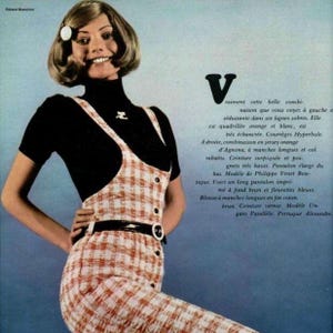 May include: A black short-sleeved turtleneck top worn under a white and orange checkered sleeveless jumpsuit. The jumpsuit features a row of black buttons down the front and a black belt with a round white buckle at the waist. The text Vraiment cette belle combi-naison que vous voyez à gauche e séduisante dans ses lignes sobres is visible.