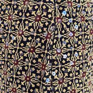 May include: A black skirt featuring a repeating geometric pattern in yellow and dark red, embellished with small, clear, circular sequins throughout the fabric. The garment includes a vertical black zipper closure centered along the back seam.