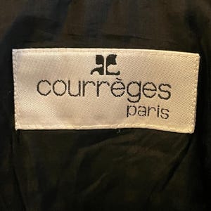May include: Close-up of a black and white houndstooth pattern fabric. A white label with the text "courr&egrave;ges paris" in black lettering is sewn onto the black lining. The Courr&egrave;ges logo is above the brand name.