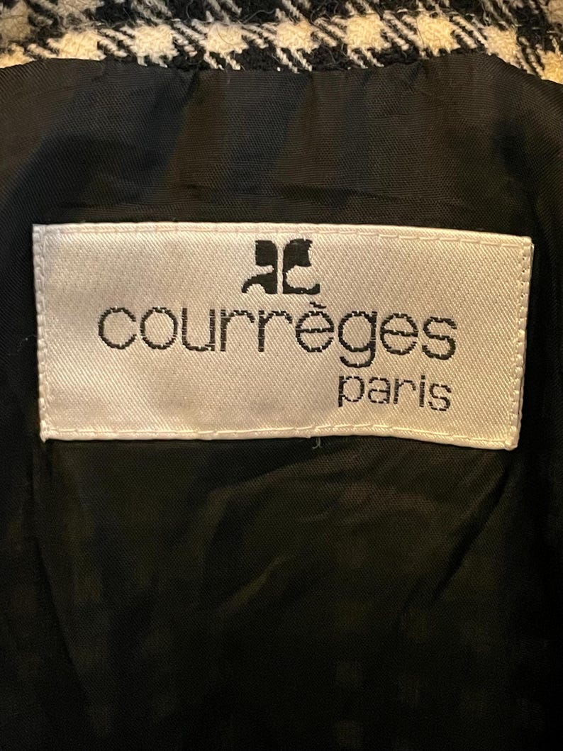May include: Close-up of a black and white houndstooth pattern fabric. A white label with the text "courr&egrave;ges paris" in black lettering is sewn onto the black lining. The Courr&egrave;ges logo is above the brand name.