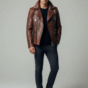 Może przedstawiać: Brązowa skórzana kurtka z fakturą skóry węża, z kołnierzem z klapami i wieloma zamkami błyskawicznymi. Połączona z czarną koszulą i ciemnoszarymi spodniami. Model nosi czarne skórzane buty. Stylowa odzież wierzchnia.