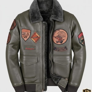 Pode incluir: Casaco de couro verde-oliva com gola de pele de carneiro e vários patches bordados. O casaco tem fecho de correr frontal, dois bolsos frontais e punhos e bainha canelados. Os patches incluem o texto "TEDMAN'S AIR COMMAND".