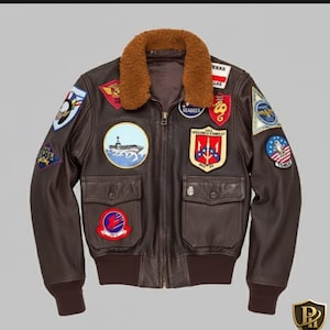 May include: A brown leather bomber jacket with a shearling collar and multiple embroidered patches. The jacket features two front pockets, a ribbed hem, and a zipper closure. Patches include military and aviation-themed designs.