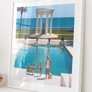 Könnte beinhalten: Ein gerahmter Druck mit einer sonnigen Außenszene. Eine Frau und ein Kind stehen mit zwei Hunden an einem Pool. Im Hintergrund befindet sich eine klassische Struktur mit Säulen und einer Statue, dahinter ist das Meer zu sehen. Das Bild ist gerahmt.