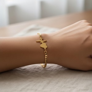 Op de afbeelding: Een goudkleurige armband met een hart- en bliksemcharm. De armband heeft een gourmette kettingontwerp en wordt om de pols gedragen. De bedel is effen goudkleurig en glanzend.
