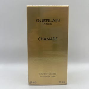 May include: A gold-coloured box of Guerlain Chamade Eau de Toilette. The box features the brand name and product name in black text. It also indicates the volume is 100 ml and 3.3 fl oz.