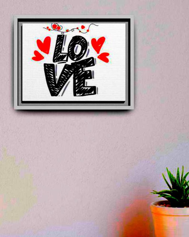 以下が含まれることがあります： 「LOVE」の文字が大きく黒い手書き文字で描かれた、額装されたキャンバスアート。赤いハートと装飾的な線が白い背景を飾っています。フレームはシルバーで、ピンク色の壁に飾られています。