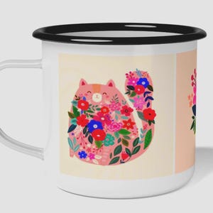K&ouml;nnte beinhalten: Ein wei&szlig;er Emaillebecher mit schwarzem Rand und Henkel, der eine grafische Illustration einer rosa Katze zeigt, die mit leuchtend roten, blauen und rosa Blumen sowie gr&uuml;nen Bl&auml;ttern auf cremefarbenem Grund bedeckt ist, mit einem Teilmotiv an der Seite.