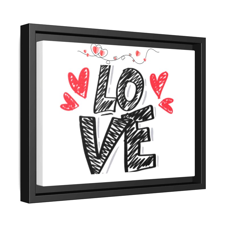 以下が含まれることがあります： 黒い落書き文字で「LOVE」という言葉が書かれた額入りのキャンバスプリント。赤いハートが単語の周りに散らばっており、ハートの細い線が文字の上部を繋いでいます。キャンバスは黒いフレームに入っています。