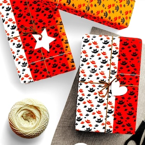 May include: Three rectangular packages wrapped in paper featuring a repeating pattern of small black and red bats. The packages are tied with brown twine and adorned with white paper gift tags shaped like a star and a heart.