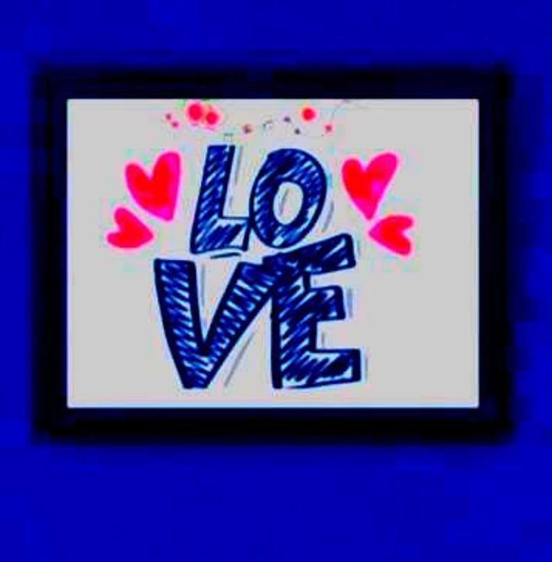 以下が含まれることがあります： 青い手書き文字で「LOVE」と書かれた額入りのアートワーク。ピンクのハートと赤い点が白い背景の周りに配置されています。黒いフレームが青い背景に映えます。