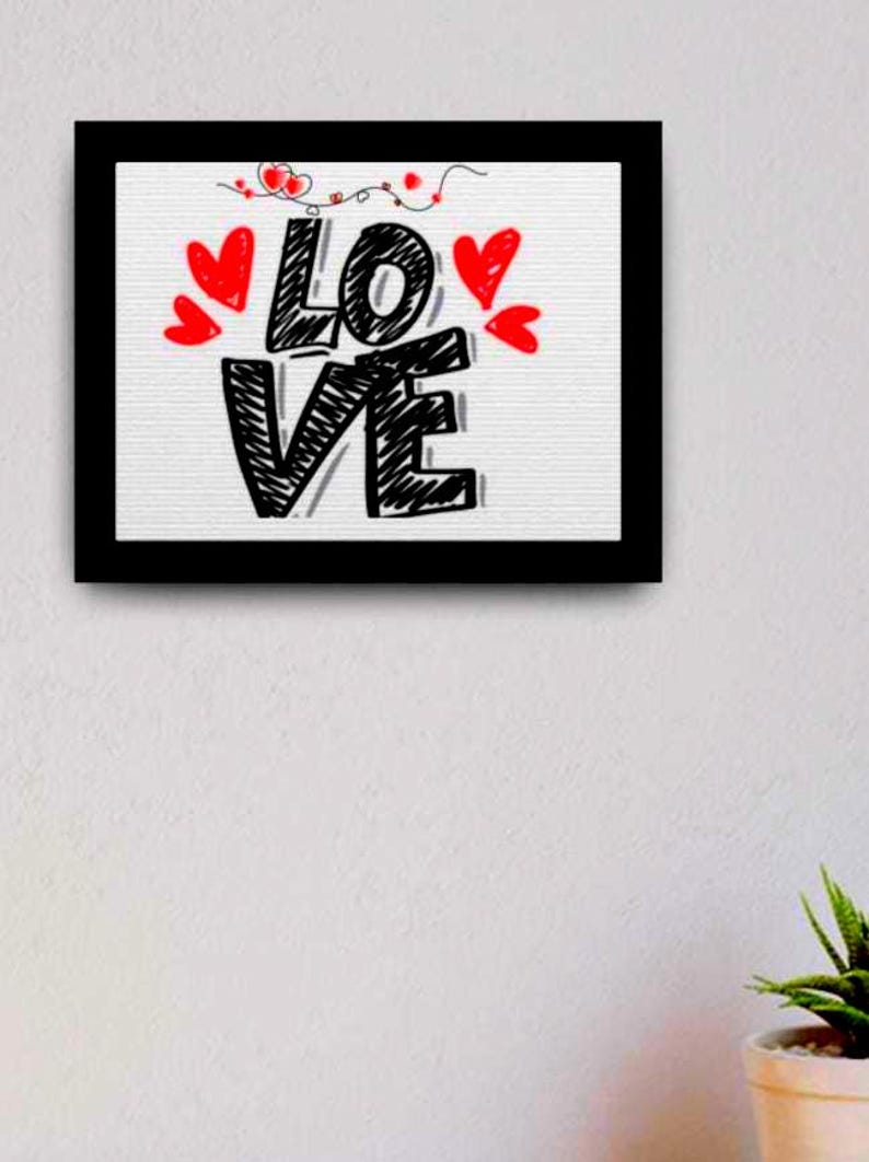 以下が含まれることがあります： 手描きのスタイルで「LOVE」という言葉が描かれた黒い額縁のアートワーク。 黒い文字は赤いハートと装飾的な要素で縁取られています。 アートワークは白い背景にあります。