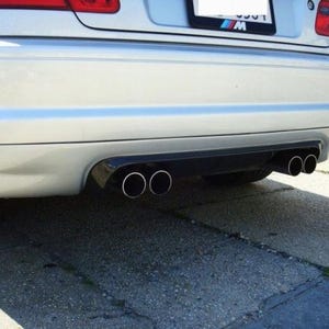 Könnte beinhalten: Silberner Stoßfänger eines Autos mit zwei Auspuffrohren. Die Auspuffrohre sind verchromt und haben ein kreisförmiges Design. Das Auto hat einen schwarzen Diffusor. Das Nummernschild ist sichtbar.