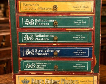 May include: A vintage wooden apothecary cabinet with six drawers. Each drawer is labeled with text such as "Browne's Eclectic Plasters" and "Belladonna Plasters." The drawers are painted in various colors, including yellow, green, and blue, with brass ring pulls.