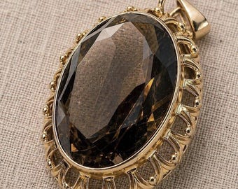 May include: An oval-shaped pendant featuring a large, faceted dark brown gemstone set in a gold-toned metal frame. The setting has an intricate, openwork scalloped border with small bead accents along the edge and a top bail for attachment.
