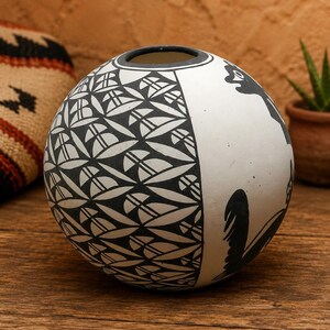 May include: A spherical ceramic vase featuring a matte white finish with contrasting black painted designs. One side displays a repeating geometric leaf pattern, while the other side features stylized black animal silhouettes.