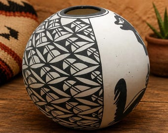 May include: A spherical ceramic vase featuring a matte white finish with contrasting black painted designs. One side displays a repeating geometric leaf pattern, while the other side features stylized black animal silhouettes.