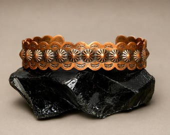 May include: A copper cuff bracelet featuring a repeating row of raised, star-shaped concho designs. The edges of the band are scalloped, and the surface is decorated with small, stamped crescent moon patterns between the central concho elements.