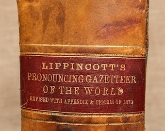 May include: An antique book spine with a weathered tan leather cover and a dark red rectangular label. The gold embossed text reads: LIPPINCOTT'S PRONOUNCING GAZETTEER OF THE WORLD, REVISED WITH APPENDIX & CENSUS OF 1870. The surface shows signs of age.