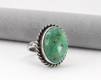 May include: A silver ring featuring a large, oval, green stone. The stone is set in a silver bezel with a twisted rope design around the edge. The ring has a detailed band with a decorative pattern.