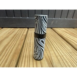 May include: A cylindrical container featuring a high-contrast black and white paisley pattern. The object consists of a main body and a matching lid, both decorated with swirling, intricate teardrop-shaped motifs that wrap around the entire surface.