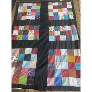 May include: A rectangular quilt featuring six distinct blocks of multi-colored fabric squares separated by solid black fabric panels. The squares display a variety of patterns including floral, plaid, polka dot, and geometric prints in many colors.