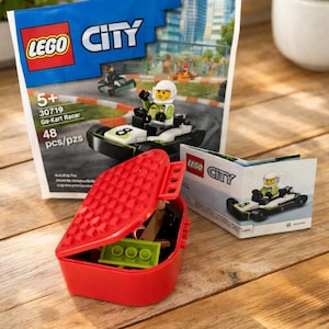 Puede incluir: Un contenedor de almacenamiento LEGO rojo con la tapa abierta, que revela varias piezas de LEGO. Una caja del set LEGO City Go-Kart Racer est&aacute; en el fondo, con un kart y un piloto. El set incluye 48 piezas.