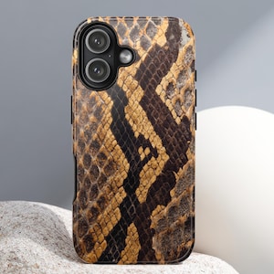 Può includere: Una custodia per smartphone con un motivo a pelle di serpente nei toni del marrone, beige e nero. La custodia ha una finitura lucida e un ritaglio per la fotocamera con due lenti.