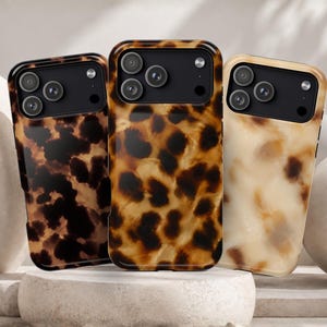 May include: Three smartphone cases featuring a glossy tortoiseshell pattern in varying shades of brown, tan, and cream. Each case has a black rectangular camera cutout section with three circular lens openings and a small circular flash aperture.