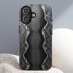 May include: A black and white snakeskin-effect phone case. The case has a textured finish and a dual-lens camera aperture. The design includes a central vertical pattern with a wavy edge, offering a strong visual contrast.