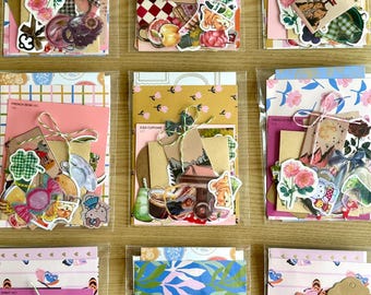 Puede incluir: Nueve bolsas de plástico transparente que contienen diversos artículos de papel, incluyendo pegatinas florales, cartulina estampada, etiquetas pequeñas y recortes decorativos. Cada conjunto está atado con cordel y presenta ilustraciones.