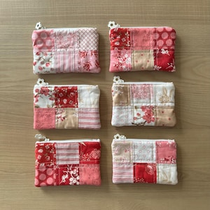 Pode incluir: Seis bolsas retangulares de tecido dispostas em duas colunas. Cada bolsa apresenta um design de patchwork com vários padrões florais, de bolinhas e listrados em vermelho, rosa e branco. Cada bolsa tem um zíper branco.