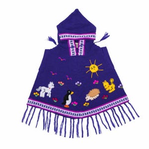Op de afbeelding: Een paarse poncho met een capuchon, met geborduurde afbeeldingen van een zon, dieren en bloemen. De poncho heeft een decoratieve rand met franjes aan de onderkant. De capuchon en rand hebben een wit en paars ontwerp.