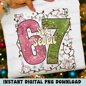 May include: White t-shirt with a festive design featuring the numbers "67" in pink and green, decorated with Christmas elements like a tree, snowman, and gifts. The words "Six Seven" are in the center. The design is surrounded by string lights and holly.