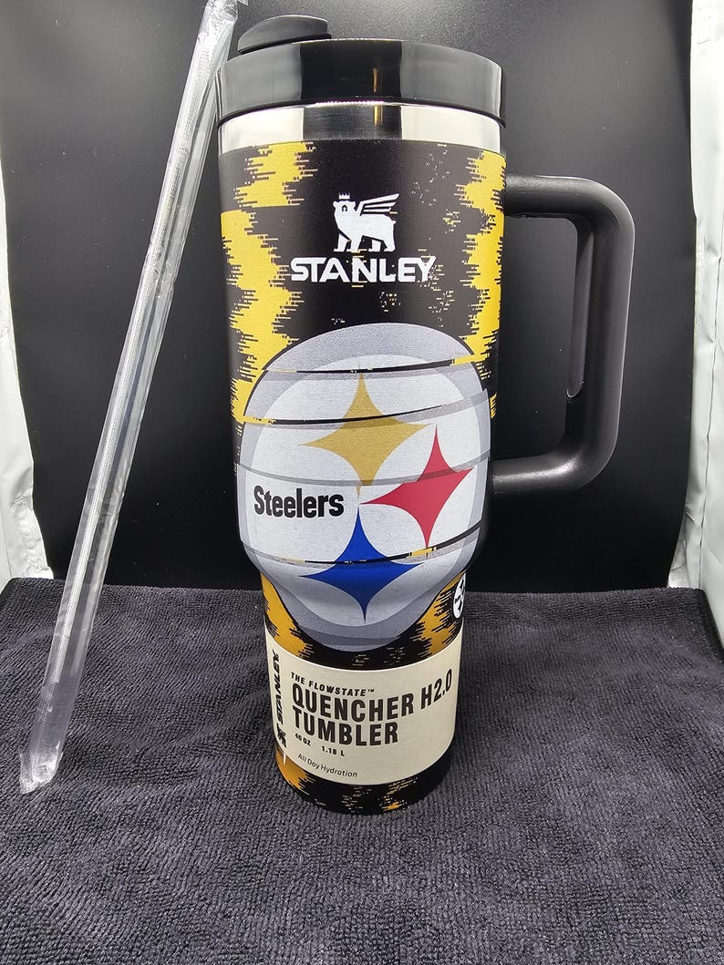 May include: Black and yellow Stanley Quencher H2.0 tumbler with a black handle and lid. The tumbler features the Pittsburgh Steelers logo and team colors. Includes a clear straw. The tumbler is designed for all-day hydration.