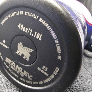 May include: Close-up of the base of a black Stanley water bottle. The bottle is marked with "40oz/1.18L" and "Designed in Seattle WA". The Stanley logo is visible, along with other text.