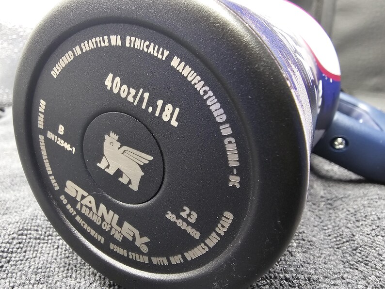 May include: Close-up of the base of a black Stanley water bottle. The bottle is marked with "40oz/1.18L" and "Designed in Seattle WA". The Stanley logo is visible, along with other text.