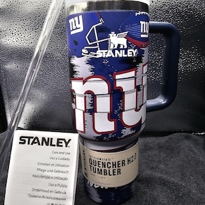 May include: A blue and white Stanley Quencher H2.0 tumbler with a handle, featuring the New York Giants logo. Includes a clear straw and a care and use booklet. The tumbler holds 1.18 litres.