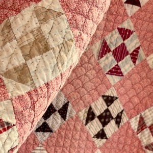 May include: A patchwork quilt featuring a repeating pattern of square blocks in various colors including red, blue, brown, and white. The fabric squares are stitched together with a textured, quilted finish throughout the entire surface.
