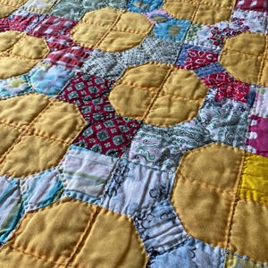 May include: A patchwork quilt featuring a repeating pattern of large solid yellow circles surrounded by smaller squares of various fabrics. The quilt displays a diverse array of colors and patterns, including red, white, blue, and green, all joined by visible stitching.