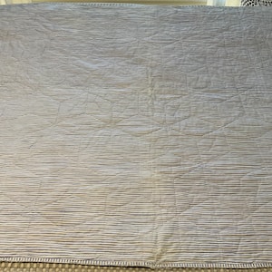 K&ouml;nnte beinhalten: Eine rechteckige Steppdecke mit einem Muster aus d&uuml;nnen, horizontalen blauen und wei&szlig;en Streifen. Die Stoffoberfl&auml;che zeigt ein dezentes, gestepptes geometrisches Design aus ineinandergreifenden Kreisen und Linien mit texturierter Optik.