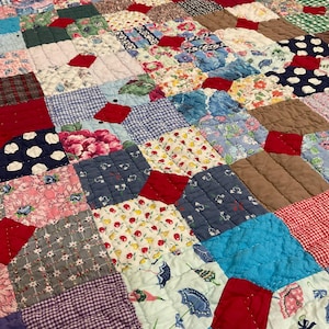 May include: A patchwork quilt with a variety of fabric patterns and colors. The quilt features squares of floral, polka dot, and gingham fabrics in shades of red, blue, pink, and green. The quilt is quilted with a diamond pattern.