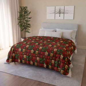 Puede incluir: Una colcha roja, verde y dorada cubre una cama. La colcha presenta un diseño cuadrado repetido con motivos de árboles de Navidad y copos de nieve. La cama está hecha con almohadas blancas y un cabecero gris claro. Un árbol decorativo y una obra de arte están en el fondo.