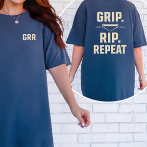 May include: Navy blue t-shirt with the text "GRR" on the front and "GRIP. RIP. REPEAT" with a baseball graphic on the back. The shirt is a short-sleeved, oversized fit.
