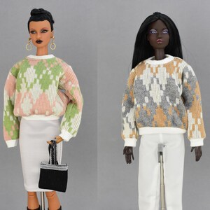 May include: Two fashion dolls are displayed, showcasing stylish outfits. One doll wears a white skirt, black boots, and a patterned sweater in green, pink, and white. The other doll is in white pants and a sweater in gray, tan, and white. The text "HOUSE OF DOUTURE" is visible.