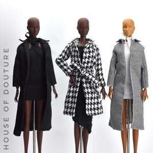 Könnte beinhalten: Drei Puppenmannequins präsentieren Miniatur-Modemäntel. Das erste Mannequin trägt einen schwarzen Mantel über einem schwarzen Kleid. Das zweite Mannequin trägt einen schwarz-weißen Hahnentrittmantel. Das dritte Mannequin trägt einen schwarz-weißen Hahnentrittmantel über einem weißen Kleid.
