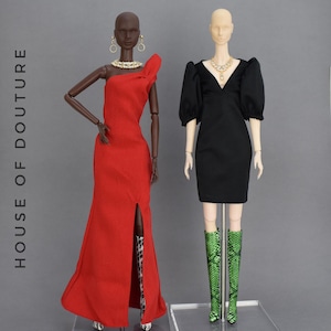 May include: Two fashion dolls are displayed. One doll wears a red, one-shoulder gown with a thigh-high slit and leopard print boots. The other doll is in a black dress with puffy sleeves and green snakeskin boots. Both dolls are accessorized with jewelry.
